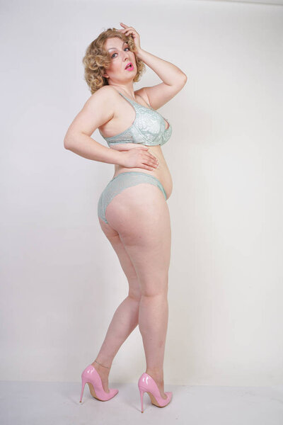 Pretty caucasian chubby woman with plus size body and pale skin wearing green lace sexy underwear on white studio background