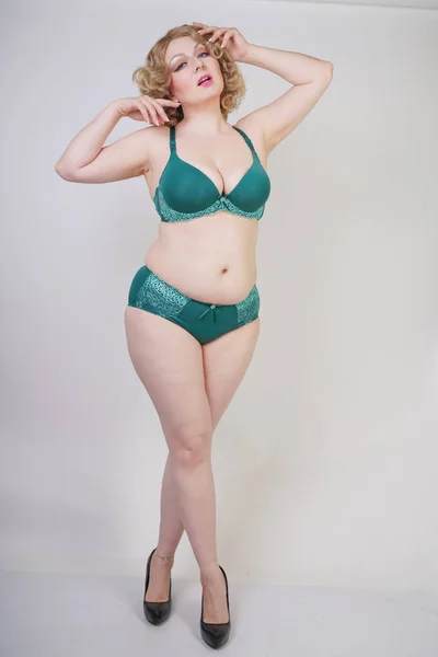 Pretty caucasian chubby woman with plus size body and pale skin wearing green lace sexy underwear on white studio background alone