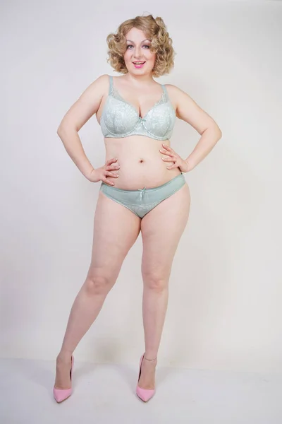 Pretty caucasian chubby woman with plus size body and pale skin wearing green lace sexy underwear on white studio background