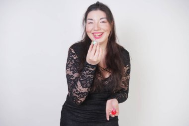 Asyalı mutlu kadın beyaz stüdyo arka plan üzerinde ruj ile dudaklarını boyar. Yanlış iyi kendini makyaj yapmaya çalışın. Yetişkin kız yüzünü boyamayı öğreniyor.