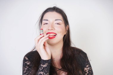 Asyalı mutlu kadın beyaz stüdyo arka plan üzerinde ruj ile dudaklarını boyar. Yanlış iyi kendini makyaj yapmaya çalışın. Yetişkin kız yüzünü boyamayı öğreniyor.