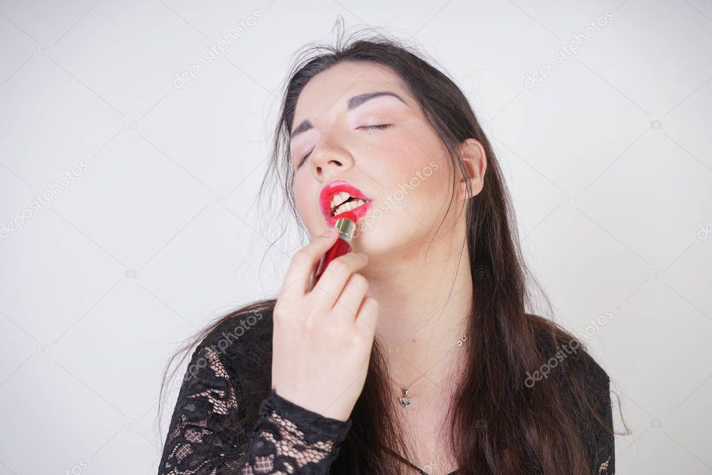 Asian happy woman paints her lips with lipstick on white studio background. Wrong try to do good self make up. Adult girl is learning to paint her face.