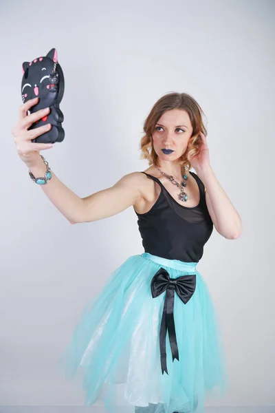 charming blonde in a bright dress with a phone in a black cat case on a white background in the Studio