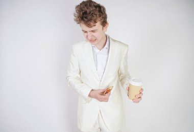 Beyaz takım elbiseli beyaz bir adam elinde bir fincan kahve ve elinde çörekle karın ağrısından muzdarip.