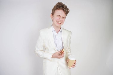 Beyaz takım elbiseli beyaz bir adam elinde bir fincan kahve ve elinde çörekle karın ağrısından muzdarip.