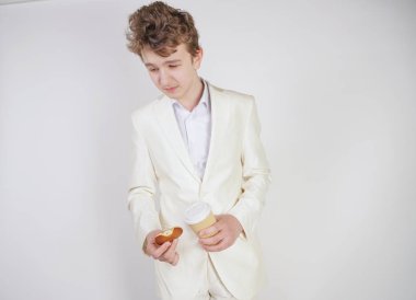 Beyaz takım elbiseli beyaz bir adam elinde bir fincan kahve ve elinde çörekle karın ağrısından muzdarip.