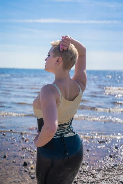 ラテックスフェティッシュ秘書のドレスを着て 一人でビーチを歩いて短いブロンドの髪を持つセクシーなホット曲線白人の女の子 — ストック写真