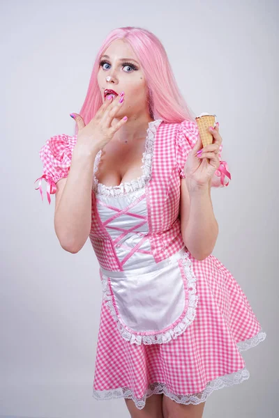 erotic caucasian chubby girl in pink plaid doll dress holds delicious summer ice cream and sexy flirts on white studio background