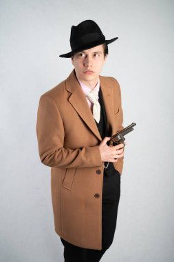 Tek başına stüdyo beyaz bir arka planda elinde bir silah ile resmi bir takım elbise ve şapka genç adam izole