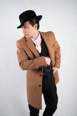 Tek başına stüdyo beyaz bir arka planda elinde bir silah ile resmi bir takım elbise ve şapka genç adam izole