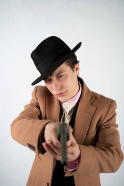 tek başına stüdyo beyaz bir arka planda elinde bir silah ile resmi bir takım elbise ve şapka genç adam