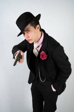 tek başına stüdyo beyaz bir arka planda elinde bir silah ile resmi bir takım elbise ve şapka genç adam