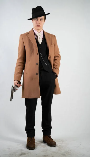 身着正式西装和帽子的年轻人手里拿着枪 在白色背景上独自在工作室里与 — 图库照片