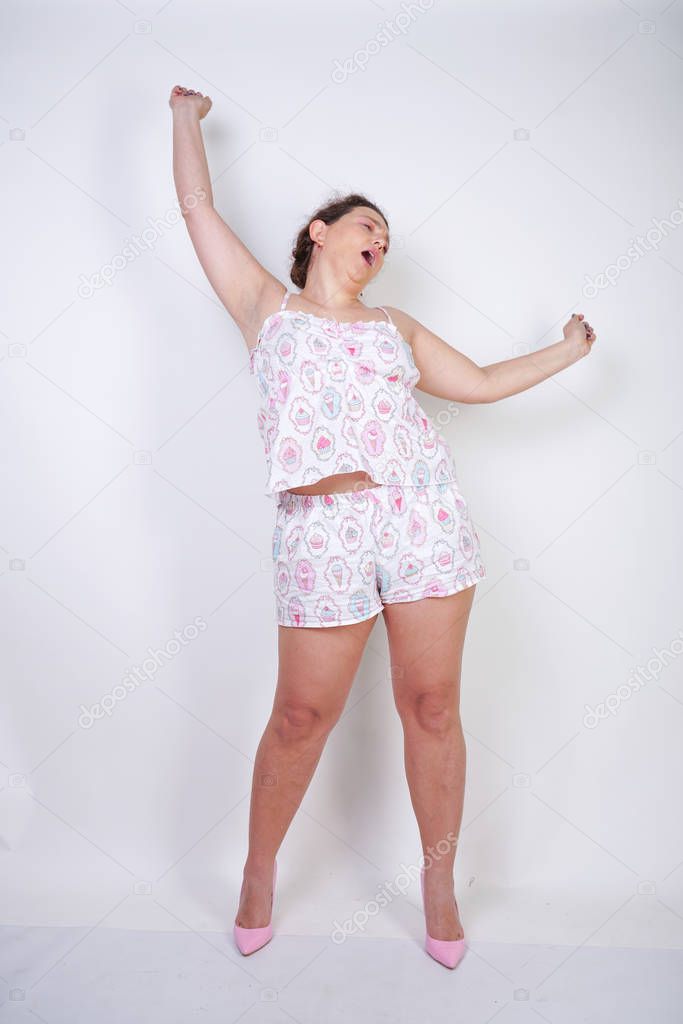chubby woman in funny pajamas stands and stretchintg on a white background in the Studio 