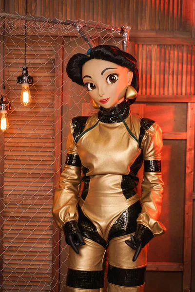 beautiful girl with full face mask doll in leather space jumpsuit posing in her room with light bulbs alone