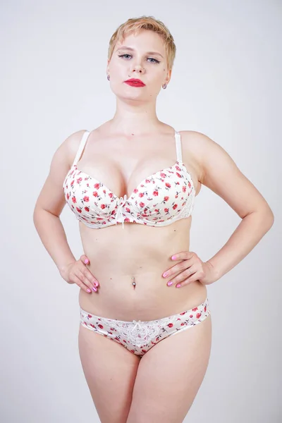 curvy caucasian short hair woman posing in cute white lingerie with red flowers print in the studio alone