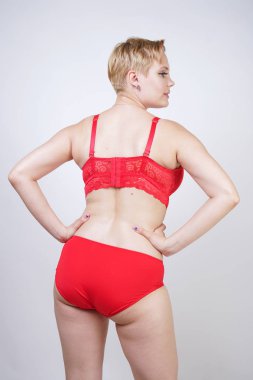 Kısa saçlı ve artı boyutunda beyaz stüdyo arka planda seksi kırmızı iç çamaşırı giyen soluk tenli güzel genç beyaz tombul kadın