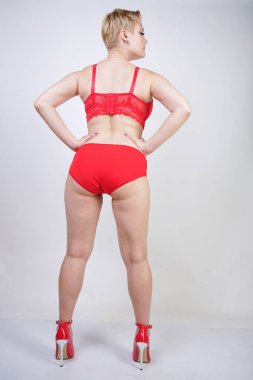 Kısa saçlı ve artı boyutunda beyaz stüdyo arka planda seksi kırmızı iç çamaşırı giyen soluk tenli güzel genç beyaz tombul kadın