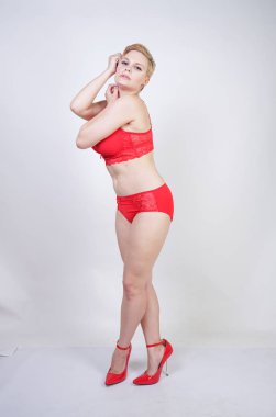 Kısa saçlı ve artı boyutunda beyaz stüdyo arka planda seksi kırmızı iç çamaşırı giyen soluk tenli güzel genç beyaz tombul kadın
