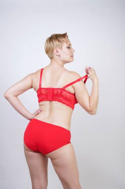 Kısa saçlı ve artı boyutunda beyaz stüdyo arka planda seksi kırmızı iç çamaşırı giyen soluk tenli güzel genç beyaz tombul kadın