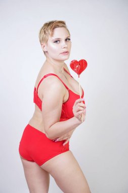 Kısa saçlı ve artı boyutunda beyaz stüdyo arka planda seksi kırmızı iç çamaşırı giyen soluk tenli güzel genç beyaz tombul kadın