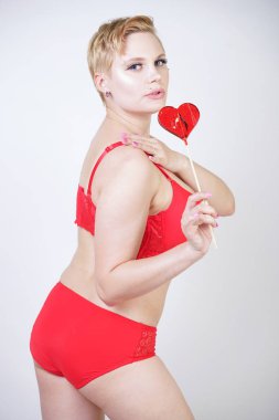 Kısa saçlı ve artı boyutunda beyaz stüdyo arka planda seksi kırmızı iç çamaşırı giyen soluk tenli güzel genç beyaz tombul kadın