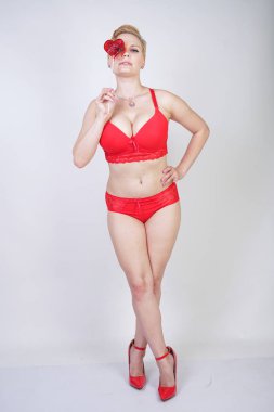 Kısa saçlı ve artı boyutunda beyaz stüdyo arka planda seksi kırmızı iç çamaşırı giyen soluk tenli güzel genç beyaz tombul kadın