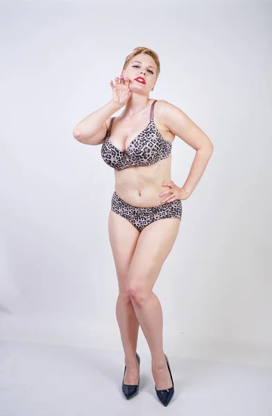 Beautiful young caucasian chubby woman with plus size body and pale skin wearing sexy lingerie with leopard print on white studio background alone