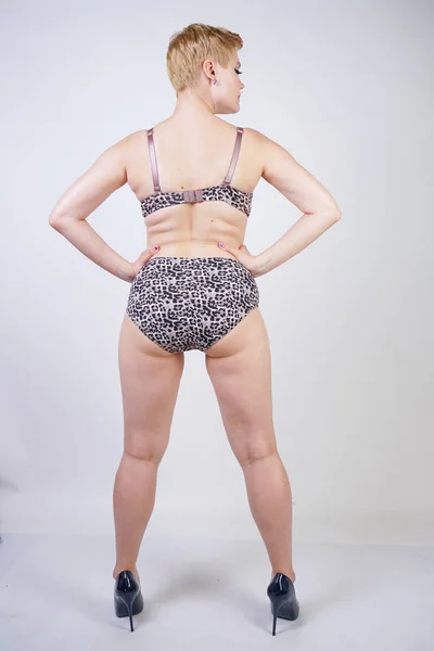 Beautiful young caucasian chubby woman with plus size body and pale skin wearing sexy lingerie with leopard print on white studio background alone