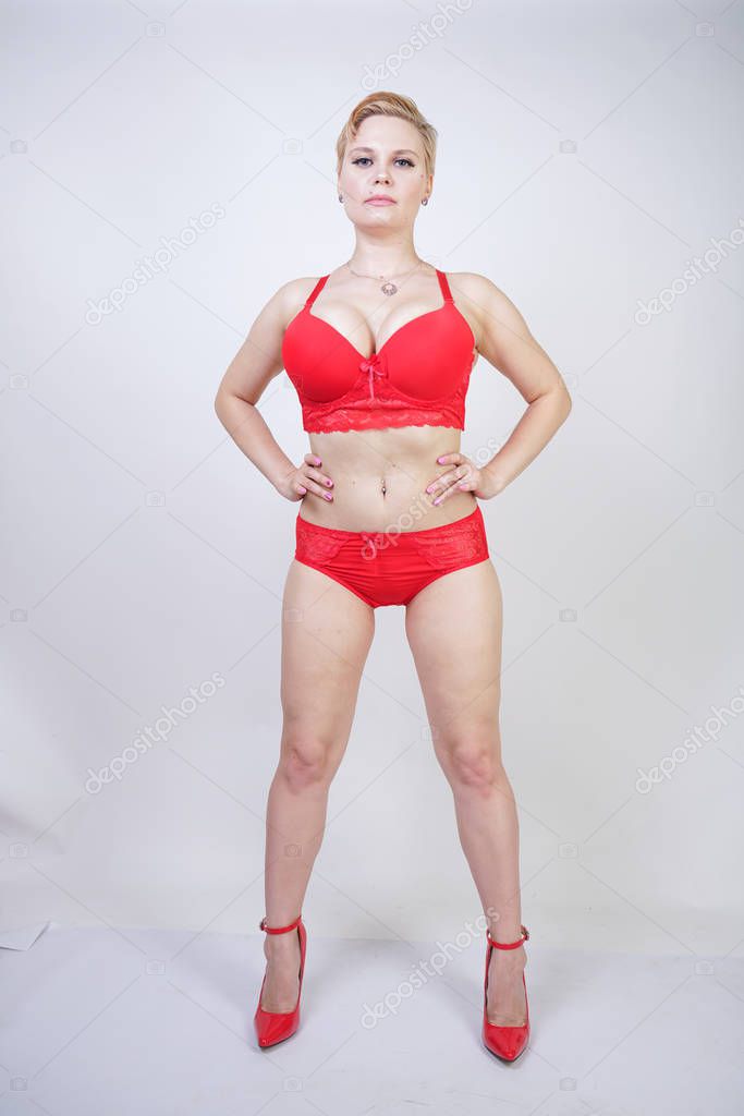 Beautiful young caucasian chubby woman with short hair and plus size body with pale skin wearing sexy red underwear on white studio background alone