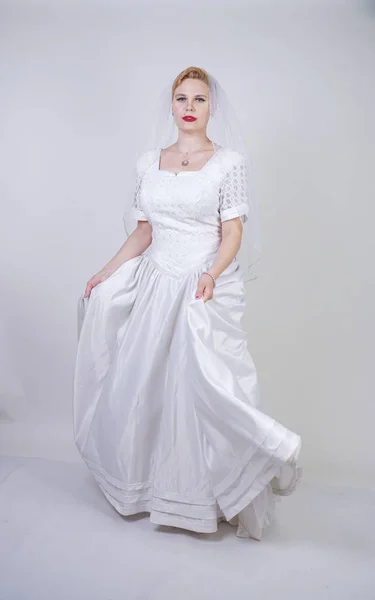 pretty curvy adult woman with short hair wearing long vintage wedding dress with sun style skirt. young caucasian bride with veil on white studio background alone.