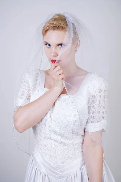 pretty curvy adult woman with short hair wearing long vintage wedding dress with sun style skirt. young caucasian bride with veil on white studio background alone.