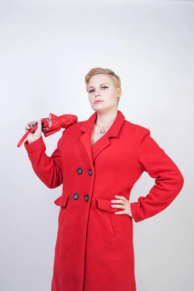 cute short hair chubby girl in a modern city wool coat holding a red umbrella and posing on a white background in the Studio alone