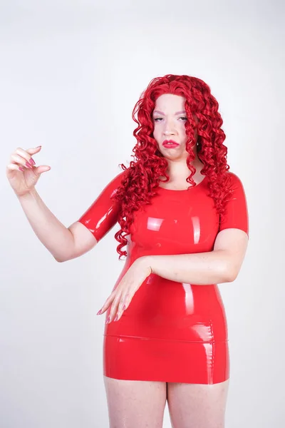 妇女显示与小阴茎的手指大小 红头发的情绪化的成年女孩与曲线身体穿着乳胶红色礼服 并有乐趣在白色工作室背景单独 — 图库照片