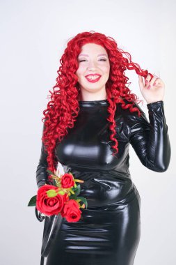 Asya yüzü ile lüks artı boyutu kadın, parlak makyaj ve kırmızı kıvırcık saç Studio beyaz arka plan üzerinde parlak kapalı uzun siyah elbise poz. ıslak bakmak sıkı giysiler ayakta sıcak yetişkin kız.