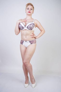 Stüdyo'da sağlam arka plan üzerinde mor dantel ile beyaz iç çamaşırı poz kısa sarı saçlı ve kıvrımlı vücut ile büyüleyici genç kadın. artı boyutu yetişkin kız iç çamaşırı giyen ve tek başına ayakta.