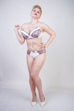 Stüdyo'da sağlam arka plan üzerinde mor dantel ile beyaz iç çamaşırı poz kısa sarı saçlı ve kıvrımlı vücut ile büyüleyici genç kadın. artı boyutu yetişkin kız iç çamaşırı giyen ve tek başına ayakta.