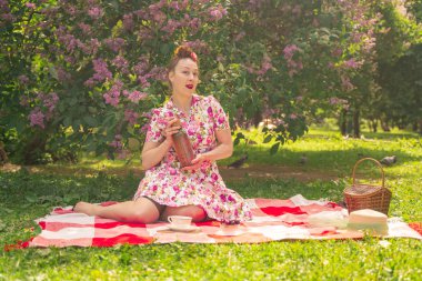 leyla çalıları yakınında Parkta damalı bir battaniye üzerinde bir yaz elbise sevgili büyüleyici pinup kız tek başına yaşam ve eğlence sahiptir. çimüzerinde oldukça mutlu beyaz kadın.