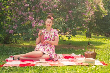 leyla çalıları yakınında Parkta damalı bir battaniye üzerinde bir yaz elbise sevgili büyüleyici pinup kız tek başına yaşam ve eğlence sahiptir. çimüzerinde oldukça mutlu beyaz kadın.