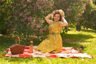 sevimli artı boyutu beyaz kız sevimli bir vintage sarı elbise giyen ve yeşil çim üzerinde yaz Parkı'nda bir tatil zevk. retro elbiseli kıvrımlı pinup kadın leylak yakın doğa üzerinde dinlenme vardır