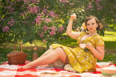 sevimli artı boyutu beyaz kız sevimli bir vintage sarı elbise giyen ve yeşil çim üzerinde yaz Parkı'nda bir tatil zevk. retro elbiseli kıvrımlı pinup kadın leylak yakın doğa üzerinde dinlenme vardır