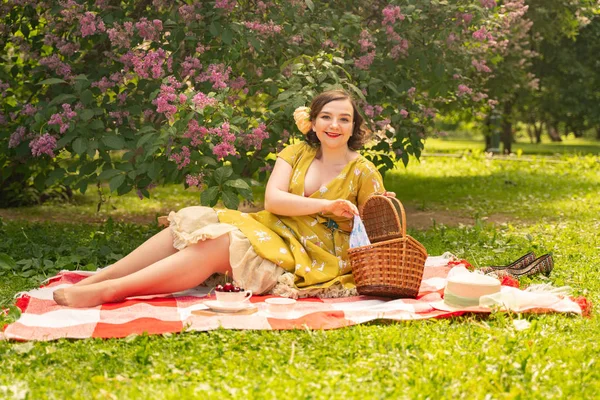 可爱加大小白种女孩穿着一个可爱的复古黄色礼服 享受在绿草的夏季公园度假 弯曲的针脚妇女复古礼服有休息附近的丁香自然 — 图库照片