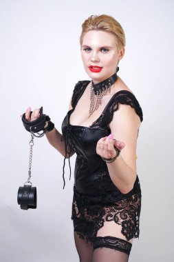 kısa sarı saçlı cryel güzel bdsm metresi siyah deri elbise ve fetiş çorap giyen ve beyaz stüdyo arka plan üzerinde tek başına zincir ile kelepçe ile poz