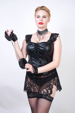 kısa sarı saçlı cryel güzel bdsm metresi siyah deri elbise ve fetiş çorap giyen ve beyaz stüdyo arka plan üzerinde tek başına zincir ile kelepçe ile poz