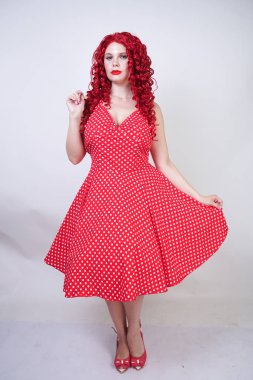 artı boyutu kırmızı saç kıvırcık kadın kıvrımlı vücut retro polka nokta güzel elbise giyen ve beyaz stüdyo arka plan tek başına ayakta. vintage giysiler poz tombul eğlenceli moda kız.
