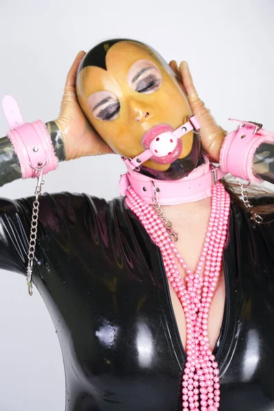 透明な顔 ゴム製のキャットスーツ Bdsmピンクの手錠と襟を持つラテックスマスクを着用ファッショナブルな大人の人 白いスタジオの背景に一人でボールギャグで遊ぶ変態スタイリッシュな女性 — ストック写真