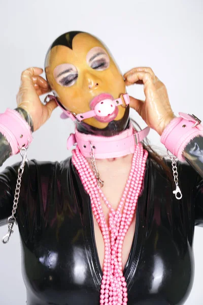 透明な顔 ゴム製のキャットスーツ Bdsmピンクの手錠と襟を持つラテックスマスクを着用ファッショナブルな大人の人 白いスタジオの背景に一人でボールギャグで遊ぶ変態スタイリッシュな女性 — ストック写真