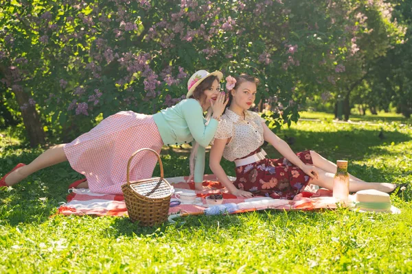 两个漂亮的女孩朋友坐在绿草上的红毯上 夏天野餐 快乐的女人有休息和乐趣 他们的空旷的自然 — 图库照片
