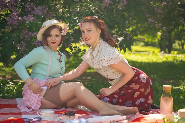 两个漂亮的女孩朋友坐在绿草上的红毯上 夏天野餐 快乐的女人有休息和乐趣 他们的空旷的自然 — 图库照片