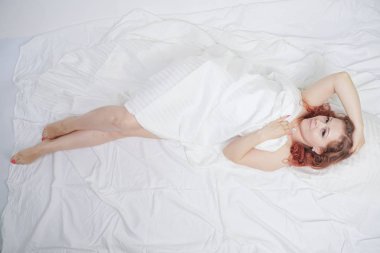 güzel genç kız beyaz bir yatakta yatıyor ve sabah zevk. büyüleyici beyaz kadın mutlu ve rahatlatıcı. uykulu ve tembel kişi yavaş yavaş tek başına poz.